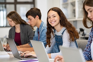 Teenager smiling while working on laptop at school